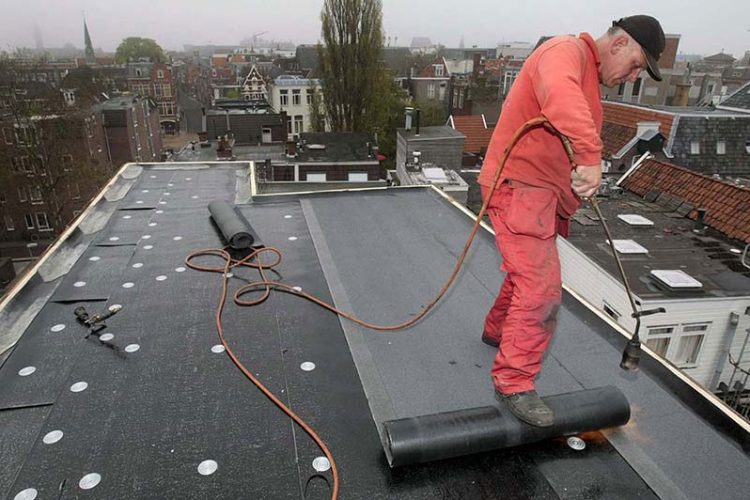 Bitumen dakbedekking uitrollen met de voet, daarlangs wordt de dakleer gebrand op het dak