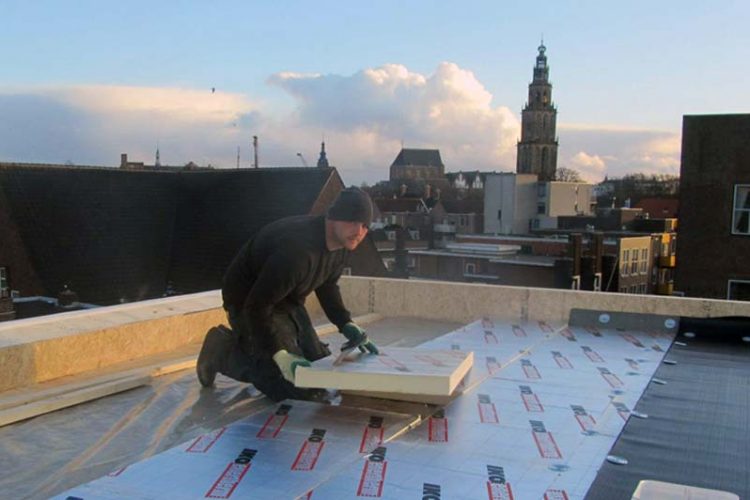 Dakisolatie platen worden aangebracht op een dak. Op de achtergrond is de martinitoren te zien